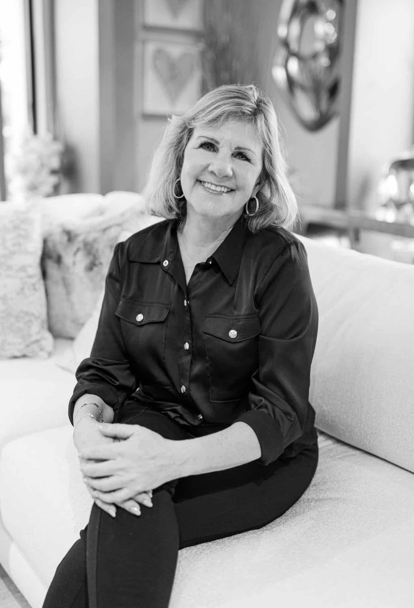 Senior woman sitting on sofa, smiling, in a cozy, styled interior.