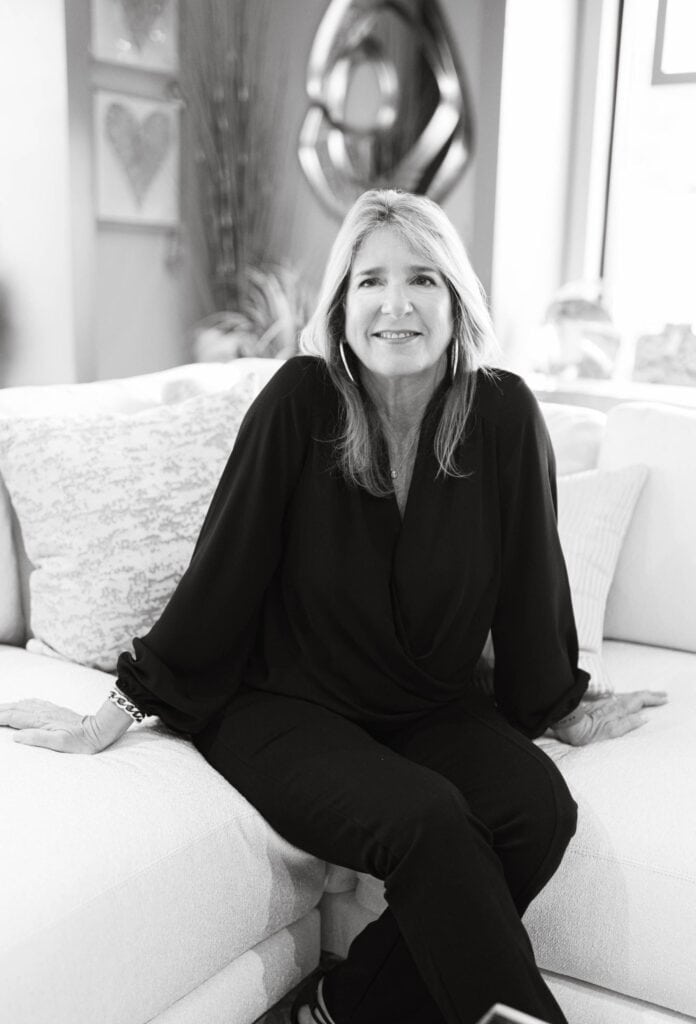Modern woman sitting on a white sofa in an art-filled living room, smiling, representing interior design and home comfort.