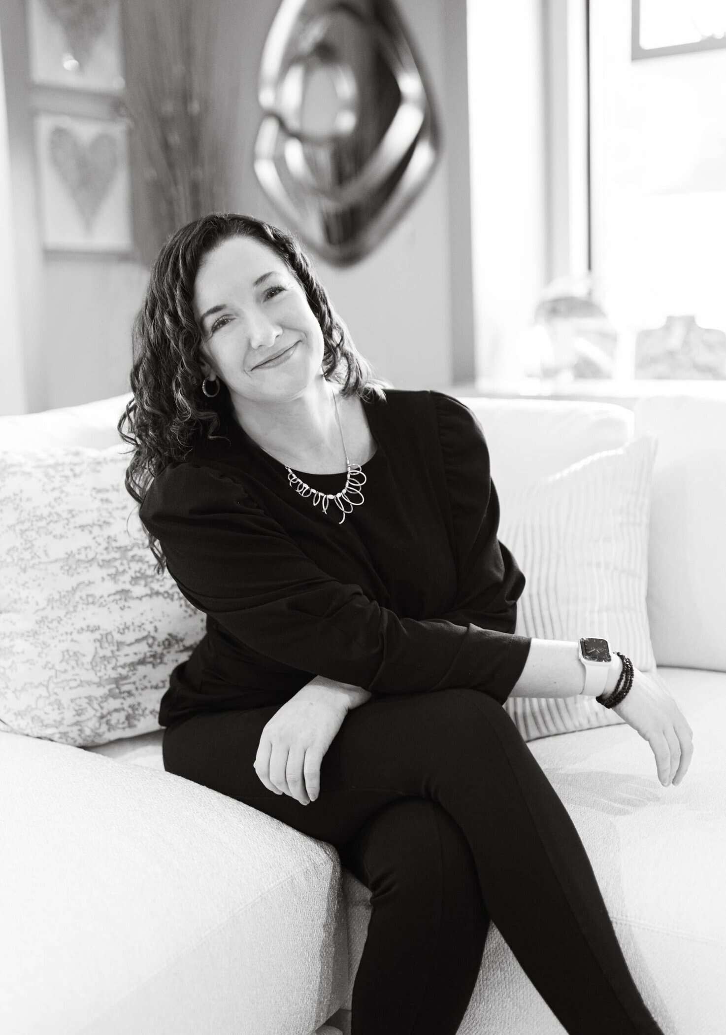 Woman sitting on a couch in a modern home, smiling.