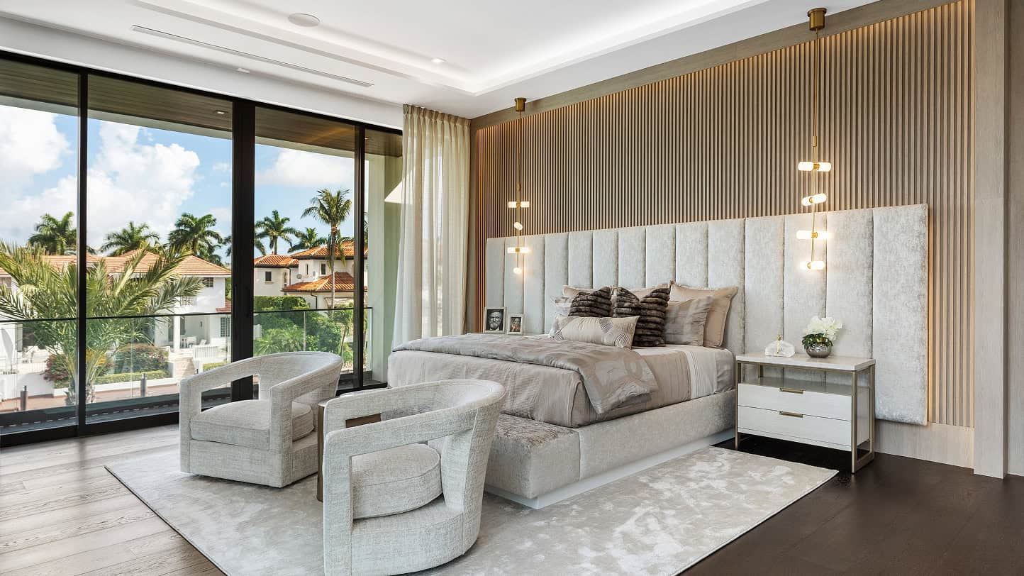 Modern luxury bedroom with custom wood paneling, plush bedding, and floor-to-ceiling windows overlooking a tropical landscape.