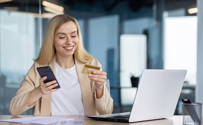 Bright young woman shopping online with credit card and smartphone in modern office environment.