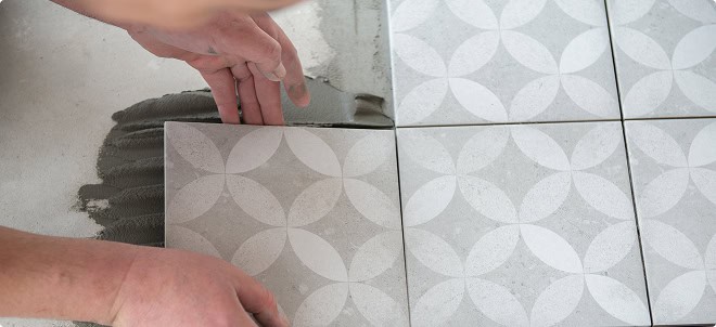 Close-up of a worker installing patterned ceramic tiles on a floor at a construction site.