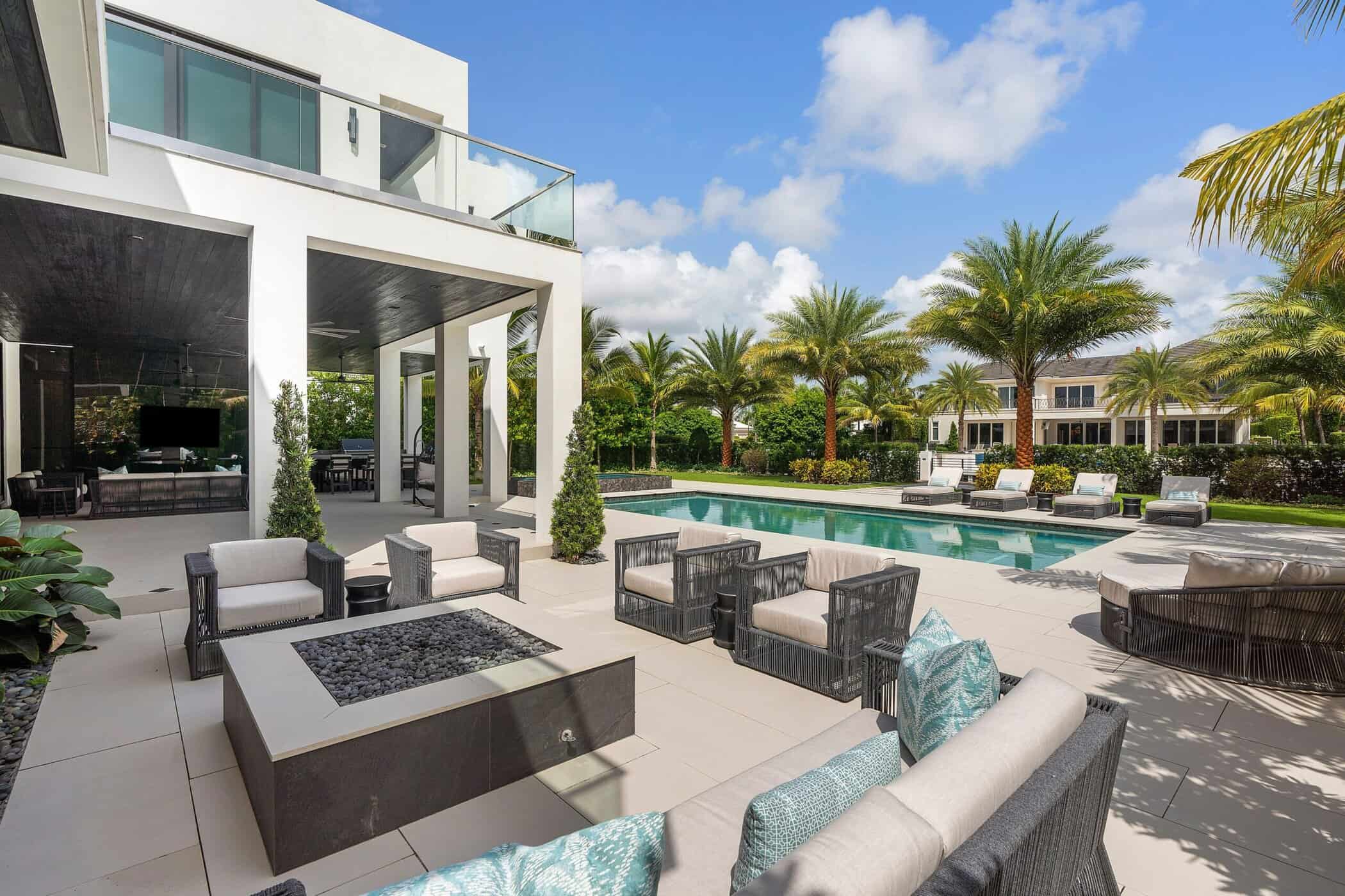 Luxury South Florida outdoor living space with swimming pool, fire pit seating, covered patio, and tropical landscaping.